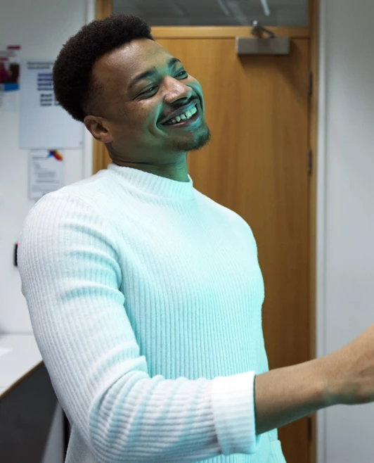 A male student in a white sweater smiles while interacting with a large touchscreen displaying months and seasons. He gestures toward the screen in a brightly lit classroom. A male student in a white sweater smiles while interacting with a large touchscreen displaying months and seasons. He gestures toward the screen in a brightly lit classroom.